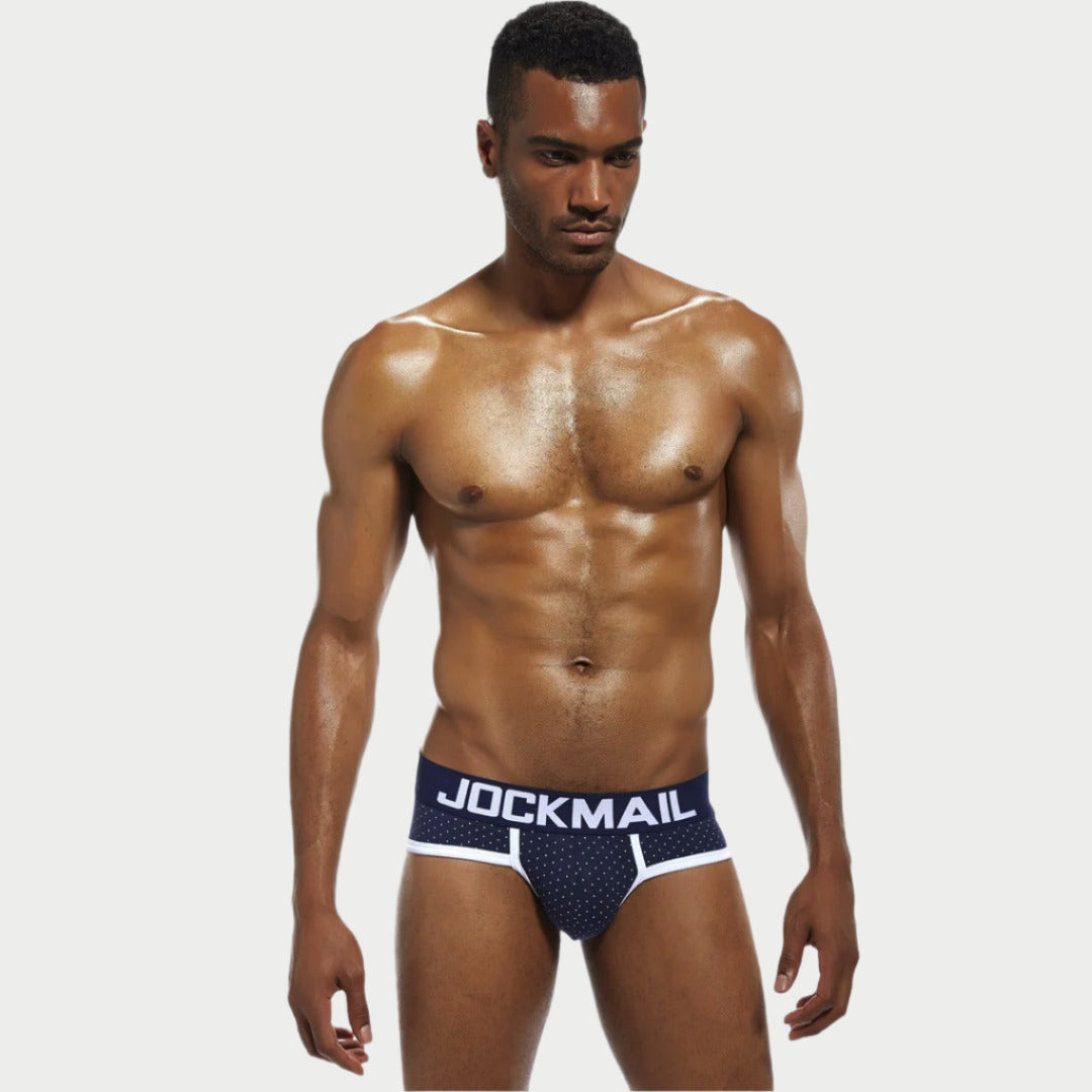 This image features a model wearing a pair of Polka Dot Cotton Briefs by JOCKMAIL. The briefs are designed with a playful polka dot pattern on the waistband, complemented by a solid navy blue color.