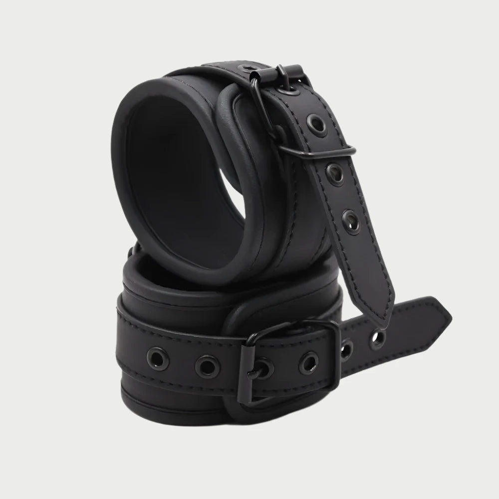A pair of black faux leather handcuffs with adjustable straps and buckle closures.