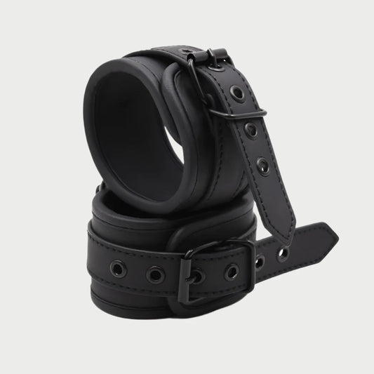 A pair of black faux leather handcuffs with adjustable straps and buckle closures.