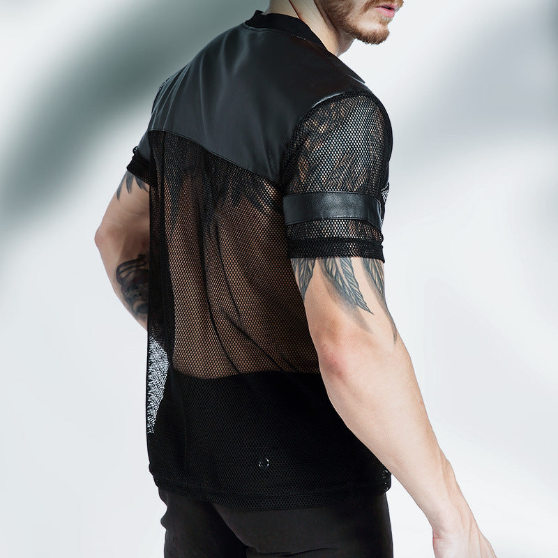 Person wearing a black mesh shirt with tattoos visible on arms against a gray background