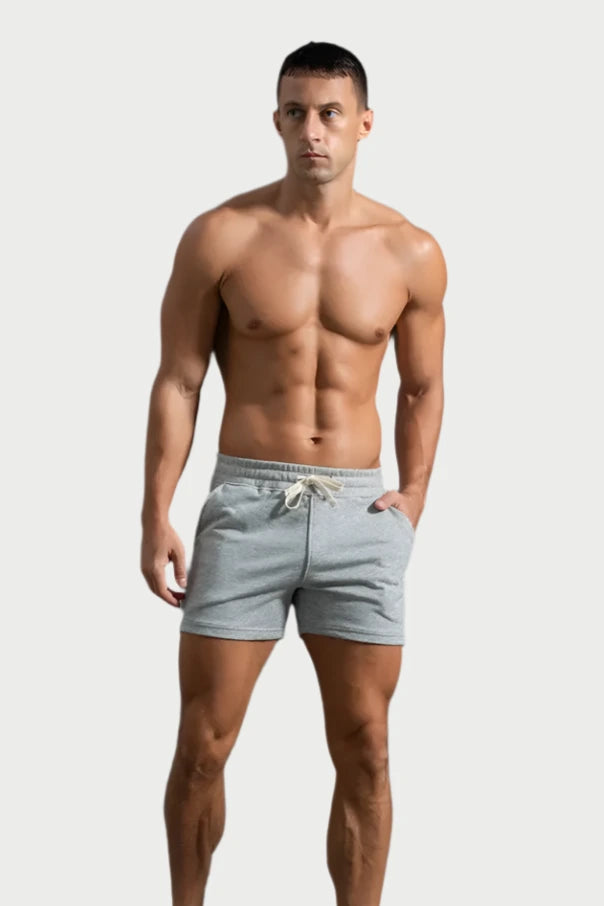 A model wearing light gray sweatpant shorts and white sneakers. The shorts are short in length, falling above the knee.