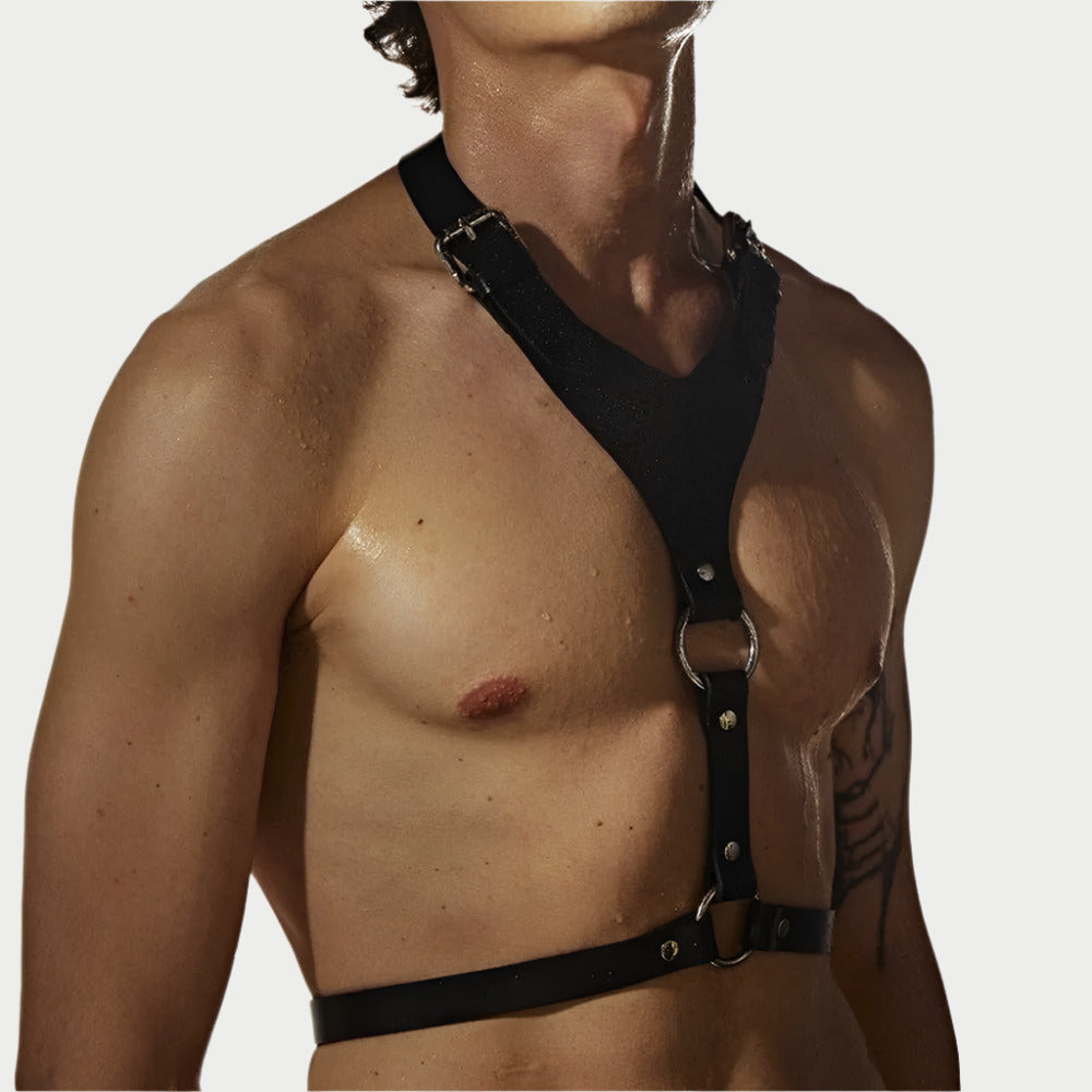 A person wearing a black faux leather chest harness with metal hardware.