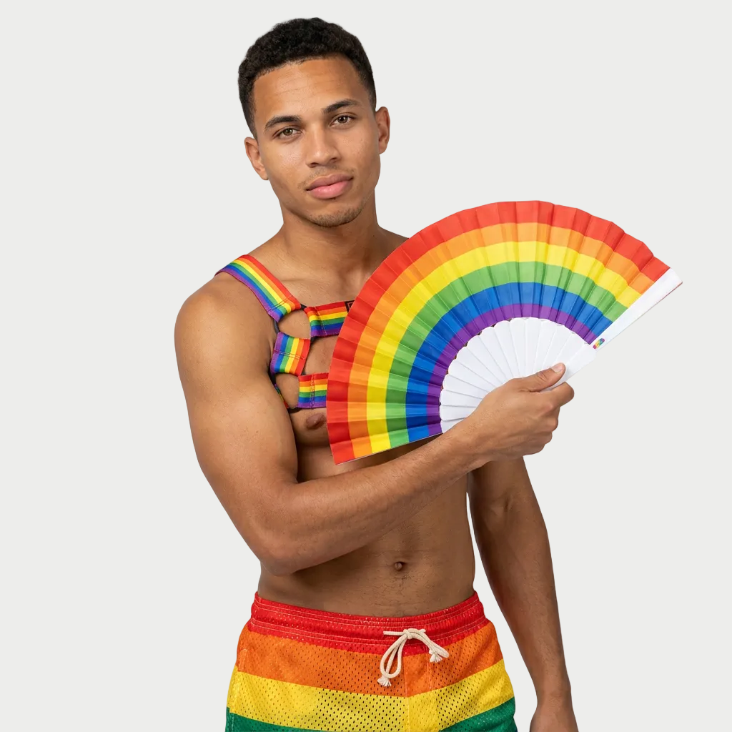 Man wearing a rainbow tank top and shorts, holding a rainbow fan against a plain background